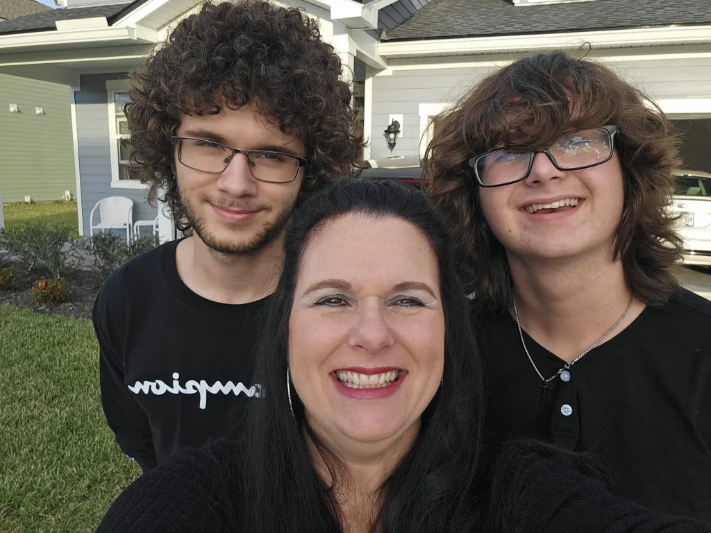 Meredith smiling with her two teenage sons outside their home on a sunny day.